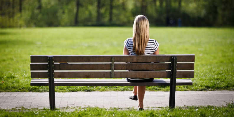 Frau sitzt mit Rücken zur Kamera auf einer Parkbank